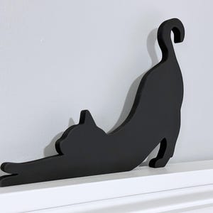 A black wooden cat silhouette wall decor. The cat is in a stretched out pose with its tail curled up.
