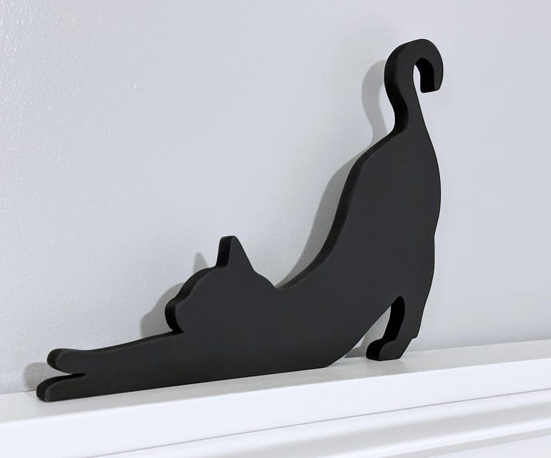 A black wooden cat silhouette wall decor. The cat is in a stretched out pose with its tail curled up.