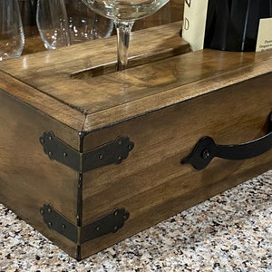 May include: Wooden wine serving tray with a dark stain, featuring a handle and decorative metal corner accents. The tray has slots for wine glasses and a bottle, ideal for serving.