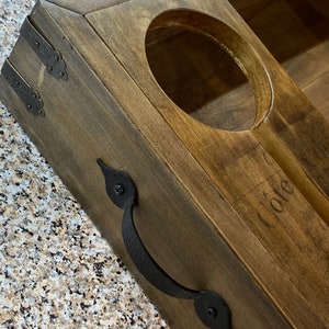 May include: A wooden wine bottle holder with a dark stain. It features a circular cutout for the bottle and a handle. The holder has decorative metal corner brackets and a handle. The word "Cote" is faintly visible.