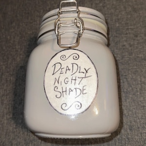 Può includere: Un barattolo di vetro grigio con un coperchio argentato e un'etichetta bianca che dice "Deadly Nightshade".