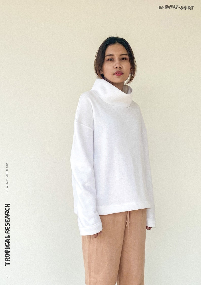May include: A person wearing a white turtleneck sweatshirt and tan drawstring trousers. The sweatshirt has a wide, folded collar and long sleeves. The text "the SWEAT-SHIRT" is in the upper right corner. The text "TROPICAL RESEARCH" is on the left side.