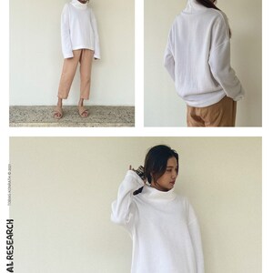 May include: A white turtleneck sweatshirt and tan trousers are shown. The sweatshirt has long sleeves and a relaxed fit. The text "the SWEAT-SHIRT" is at the top right. The text "TROPICAL RESEARCH" is on the left side.