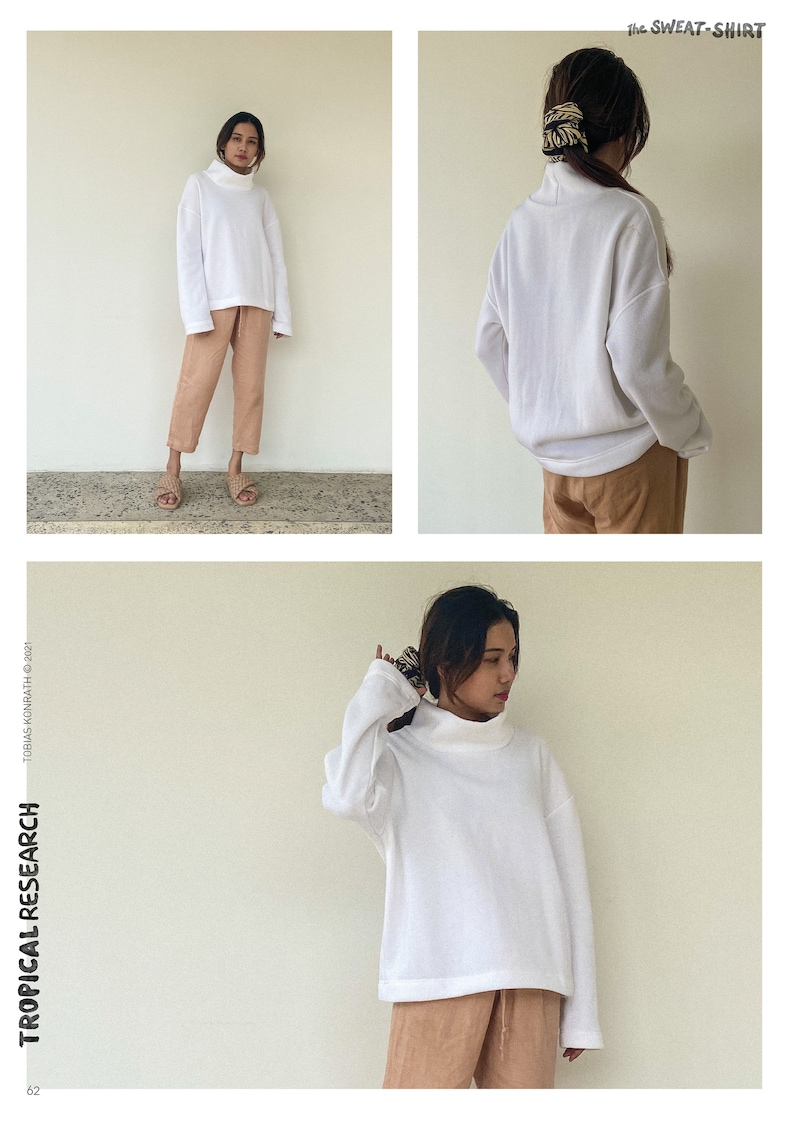 May include: A white turtleneck sweatshirt and tan trousers are shown. The sweatshirt has long sleeves and a relaxed fit. The text "the SWEAT-SHIRT" is at the top right. The text "TROPICAL RESEARCH" is on the left side.