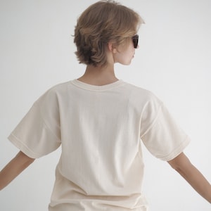 May include: A woman wearing a plain, off-white t-shirt with short sleeves. The t-shirt is made of a soft, comfortable fabric.
