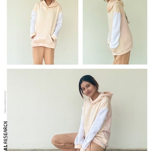 May include: A peach-coloured hoodie with white sleeves and a front pocket, worn with matching peach-coloured trousers. The sweatshirt has a hood. The text "TROPICAL RESEARCH" is visible. The image also includes the text "the SWEAT-SHIRT".