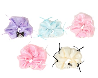 Può includere: Un set di cinque elastici per capelli in raso nei colori viola, azzurro, rosa e crema. Ogni elastico presenta sottili nastri e un piccolo ciondolo a forma di personaggio, tra cui Kuromi, Cinnamoroll, My Melody e Hello Kitty, in cerchio.