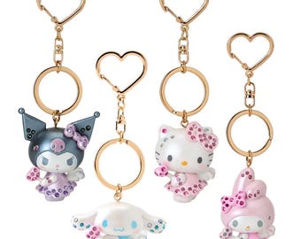 May include: Four colorful character keychains with jeweled accents. The keychains feature Hello Kitty, My Melody, and two Kuromi characters. Each keychain has a gold heart-shaped ring and a gold chain.