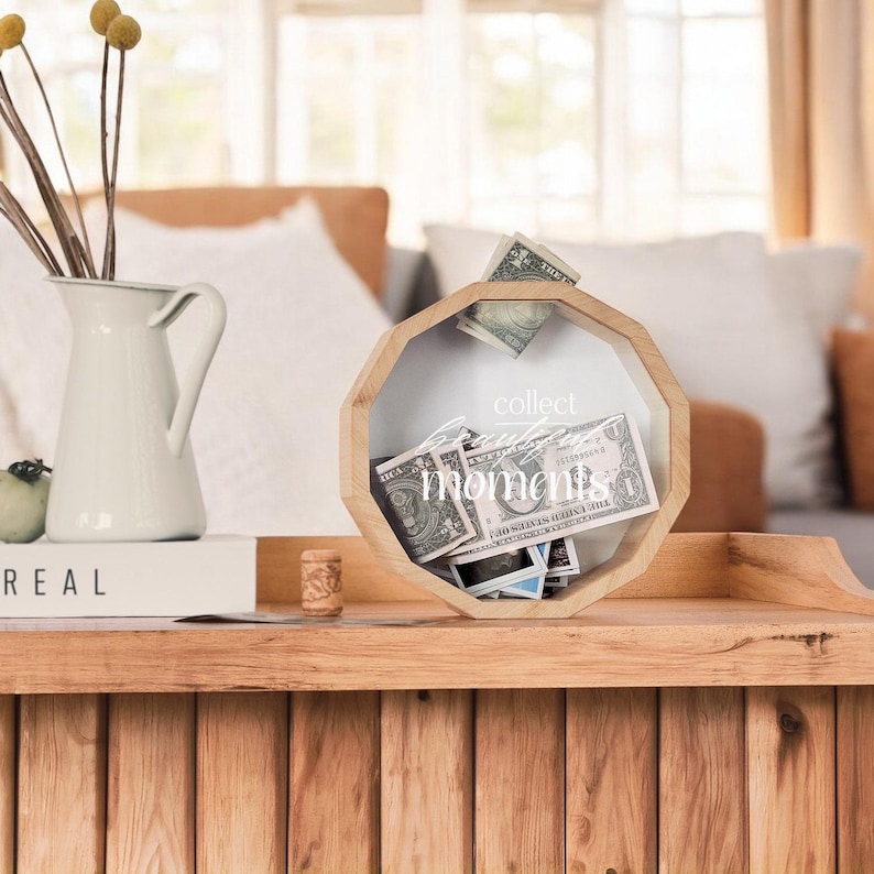 May include: A wooden octagonal box with a glass front. The box has a white inscription that reads "collect moments". The box is filled with cash and photos.