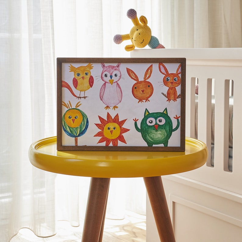 Puede incluir: Una impresi&oacute;n enmarcada con una ilustraci&oacute;n colorida de varios animales, incluyendo b&uacute;hos, un p&aacute;jaro, una flor y una ardilla. La impresi&oacute;n est&aacute; sobre una mesa amarilla con un fondo blanco.