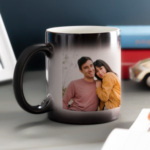 May include: Black magic mug with a photo of a couple smiling and hugging. The mug changes color when hot.