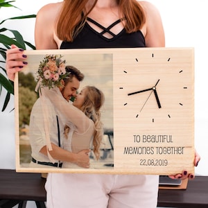 Puede incluir: Un reloj de madera con una fotografía de una pareja abrazándose, con un ramo de flores. La esfera del reloj tiene manecillas y marcadores de minutos negros. El texto en el reloj dice "TO BEAUTIFUL MEMORIES TOGETHER 22.08.2019."