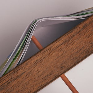 Puede incluir: Primer plano de un marco de madera con una pila de papeles en su interior. Los papeles est&aacute;n doblados por la mitad y tienen un patr&oacute;n verde y blanco.