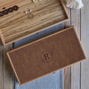 May include: A wooden backgammon game set with a brown leatherette lid featuring a monogrammed initial "R" in a circle with floral accents.
