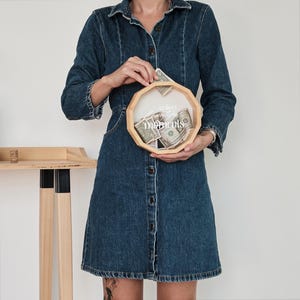 May include: A wooden money box with a clear glass top and the text "collect moments" printed on the front. The box is filled with US dollar bills. A person is holding the box in their hands.