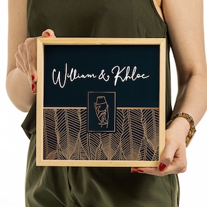 May include: A square wooden frame containing a dark navy blue sign with the white text William & Khloe. The design features a central copper-colored line art illustration of a hand holding a glass, set against a background of copper leaf patterns.