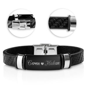 Könnte beinhalten: Schwarzes Lederarmband mit einem silbernen Verschluss und einer silbernen Platte, die mit dem Text "Ceren ♥ Hakan" graviert ist.