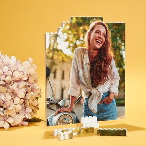 May include: A woman smiles while leaning against a vintage motorcycle. The image is made up of small square tiles, like a mosaic.