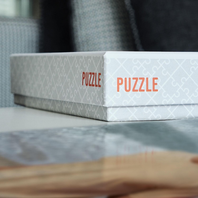 May include: A white box with a gray and white puzzle pattern and the word "PUZZLE" printed in orange on the front and side.