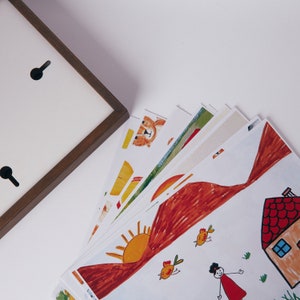 Puede incluir: Una pila de tarjetas blancas con dibujos coloridos de una casa, un sol, p&aacute;jaros y un oso. Las tarjetas est&aacute;n abiertas en abanico y dispuestas en semic&iacute;rculo.