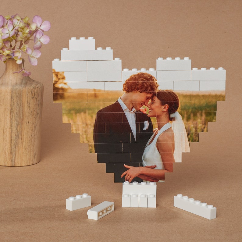May include: A white LEGO heart frame with a photo of a couple in love. The couple is standing in a field and looking at each other. The photo is surrounded by white LEGO bricks.