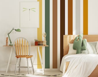 May include: A bedroom with a white wall, a wooden bed with a white duvet and green cactus pillows, a white desk with a wooden chair, a green lamp, and a framed print of a dragonfly. The wall has vertical stripes in yellow, green, brown, and gray.