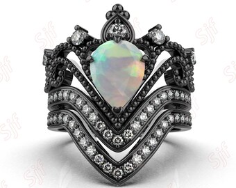 May include: A black and white ring featuring a pear-shaped opal gemstone set in a crown-shaped design. The ring is embellished with smaller white gemstones.