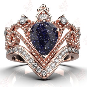 May include: A rose gold ring with a blue pear-shaped gemstone surrounded by smaller diamonds. The ring features a crown-like design with intricate details.