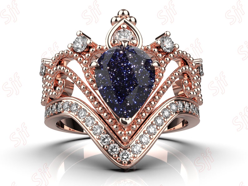 May include: A rose gold ring with a blue pear-shaped gemstone surrounded by smaller diamonds. The ring features a crown-like design with intricate details.