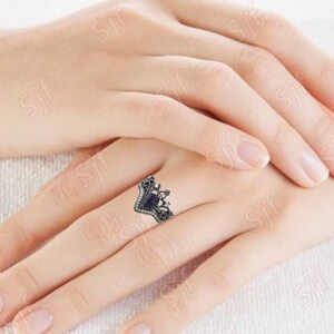 May include: A silver ring with a black heart-shaped stone surrounded by smaller stones. The ring is on a finger.