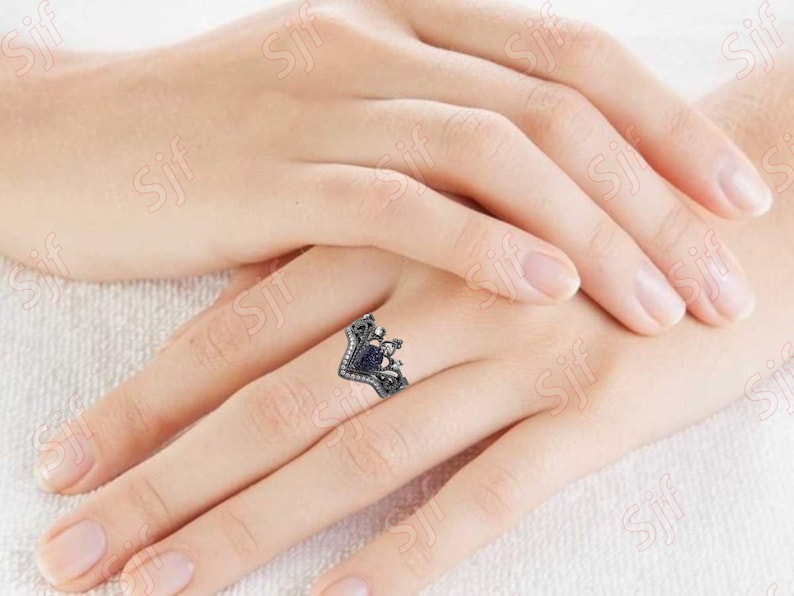 May include: A silver ring with a black heart-shaped stone surrounded by smaller stones. The ring is on a finger.