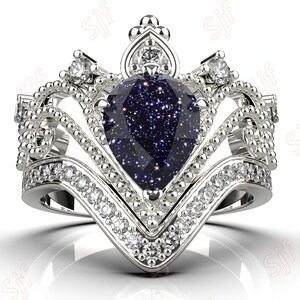 May include: A silver ring with a large blue pear-shaped gemstone surrounded by smaller clear gemstones. The ring is designed in a crown shape with intricate details.