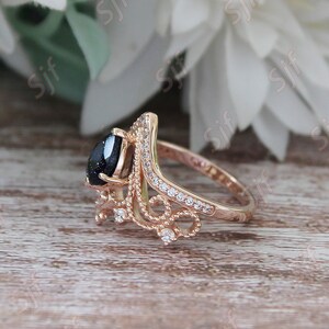 May include: A rose gold ring with a black gemstone and a delicate, ornate design. The ring is set with small, clear stones.