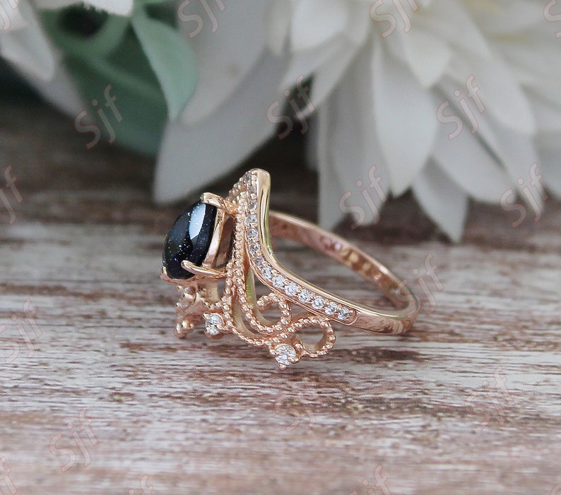 May include: A rose gold ring with a black gemstone and a delicate, ornate design. The ring is set with small, clear stones.