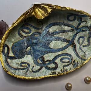 May include: A seashell dish with a gold rim and a blue and white octopus painted on the inside. The octopus has many tentacles and is curled up in the center of the dish.