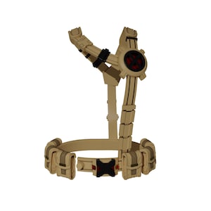 May include: Tan-colored tactical harness with a belt featuring pouches and a central buckle. The harness has a circular element with a red center and black accents. The design includes adjustable straps and multiple attachment points.