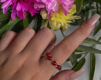 May include: A silver ring with a row of red carnelian beads. The ring is on a person's finger.
