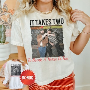 Puede incluir: Una camiseta blanca con un gráfico desgastado de dos hombres con el texto "IT TAKES TWO To Break A Heart In Two".