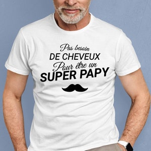 May include: White t-shirt with black text that reads "Pas besoin de cheveux pour &ecirc;tre un SUPER PAPY" and a black mustache graphic.