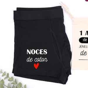 Könnte beinhalten: Schwarze Boxershorts mit dem Text "NOCES de coton" und einem roten Herz. Ein kleiner beiger Kordelzugbeutel mit dem Text "1 ANNÉE de mariage" und "JOYEUSES NOCES de coton" ist ebenfalls vorhanden.