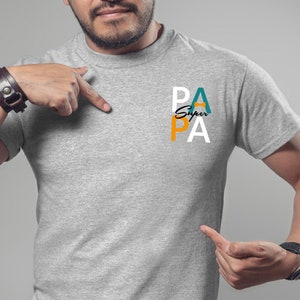 以下が含まれることがあります： 白、オレンジ、ターコイズで「スーパーパパ」とプリントされたグレーのTシャツです。