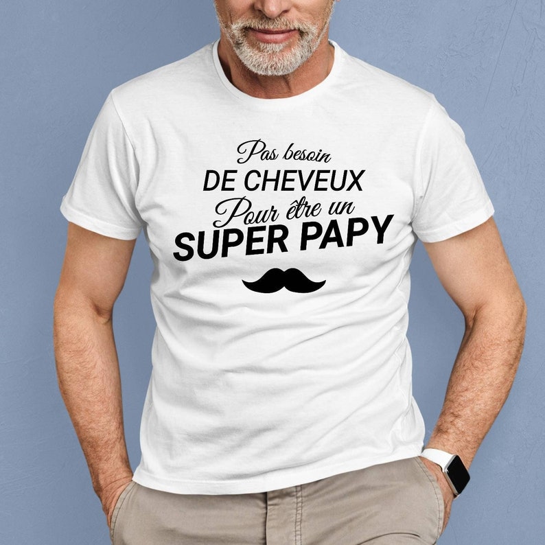 May include: White t-shirt with black text that reads "Pas besoin de cheveux pour &ecirc;tre un SUPER PAPY" and a black mustache graphic.