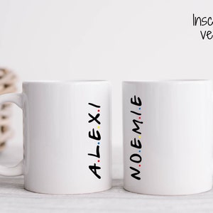 Peut inclure: Deux tasses en céramique blanche avec du texte noir qui dit "ALEXI" et "NOEMIE" en format vertical et empilé. Le texte est décoré de points colorés.