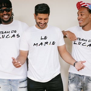 K&ouml;nnte beinhalten: Drei Personen tragen wei&szlig;e T-Shirts mit schwarzem Text. Ein Shirt tr&auml;gt die Aufschrift "LE MARIE" und die beiden anderen "TEAM DE L.U.C.A.S" in einer Schriftart, die der Fernsehserie Friends &auml;hnelt. Die Shirts sind f&uuml;r einen Junggesellenabschied.