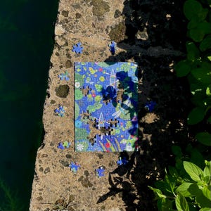 May include: A rectangular jigsaw puzzle featuring a vibrant blue and green illustration of dragonflies, water lilies, and small white boats. The puzzle is partially assembled with several loose pieces scattered around the main rectangular section.