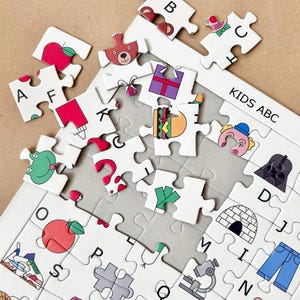 May include: A colorful alphabet puzzle with images for each letter. The puzzle pieces are scattered on a gray surface. The puzzle is labeled "KIDS ABC".