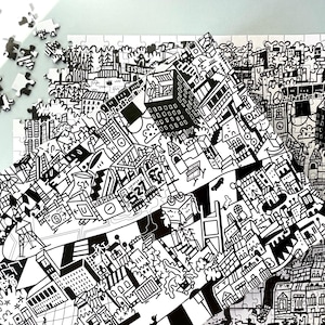 Puede incluir: Rompecabezas en blanco y negro que representa una escena de ciudad con edificios, árboles y otros detalles. El rompecabezas está parcialmente ensamblado, mostrando el diseño intrincado.