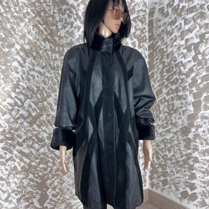 May include: A black leather coat with a high collar and fur trim on the collar and cuffs. The coat features a diamond pattern design on the front and sleeves. The coat is knee-length and has a button closure.