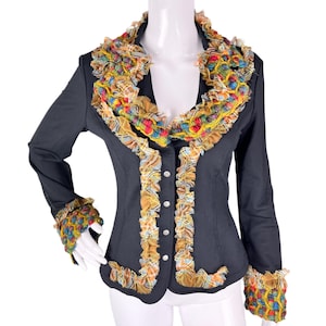 Puede incluir: Una blazer gris oscuro con cuello, puños y ribete con volantes de colores. La chaqueta presenta un cuello en V, mangas largas y botones plateados en la parte delantera. Los volantes incorporan tonos amarillos, azules, rojos y naranjas.