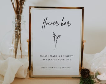 May include: A gold-framed sign with the text "Flower Bar" and instructions to "Please make a bouquet to take on your way." The sign also includes the text "emily's bridal shower | 10.04.2024".
